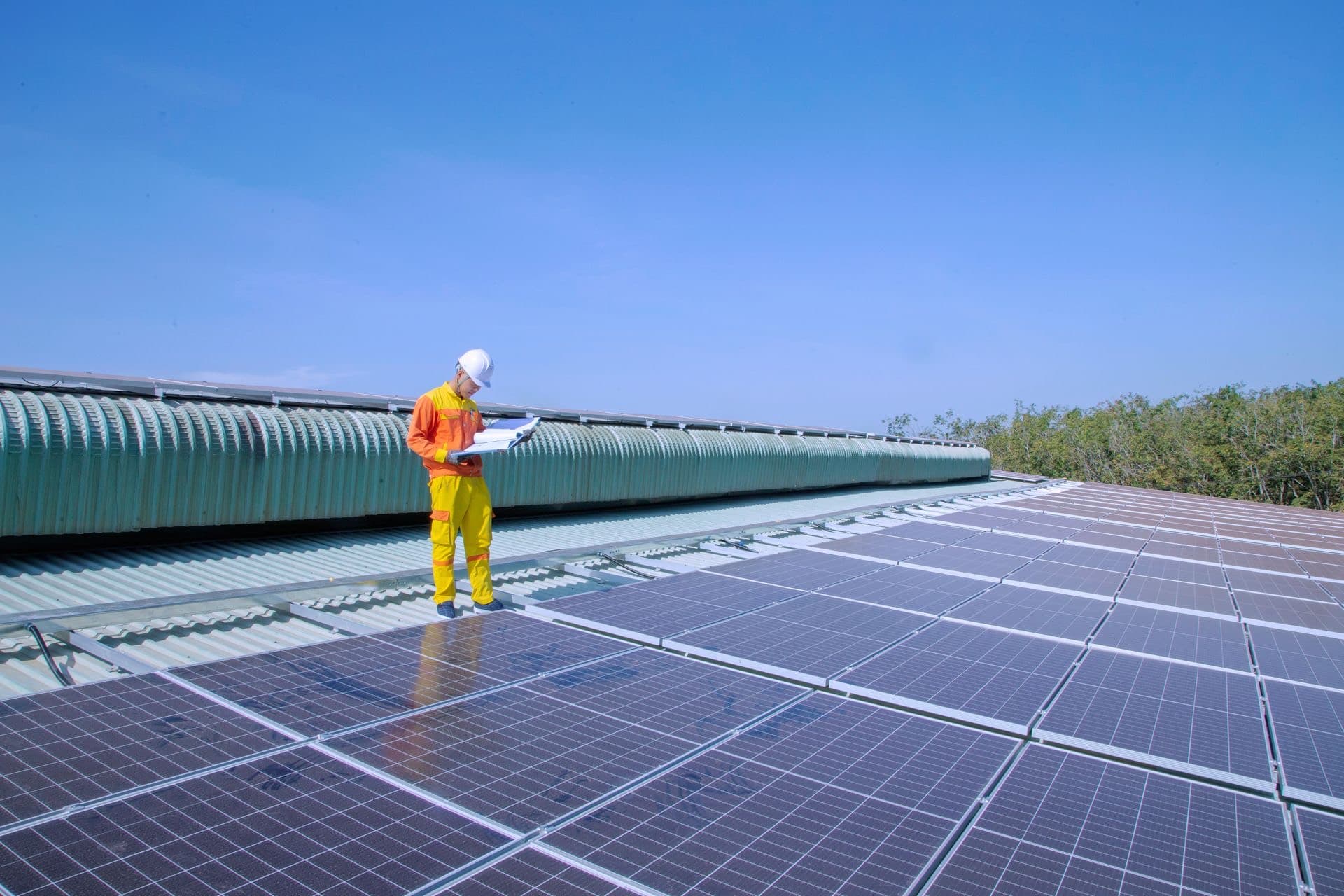 Engineer inspecting a commercial rooftop solar array under a deep blue sky