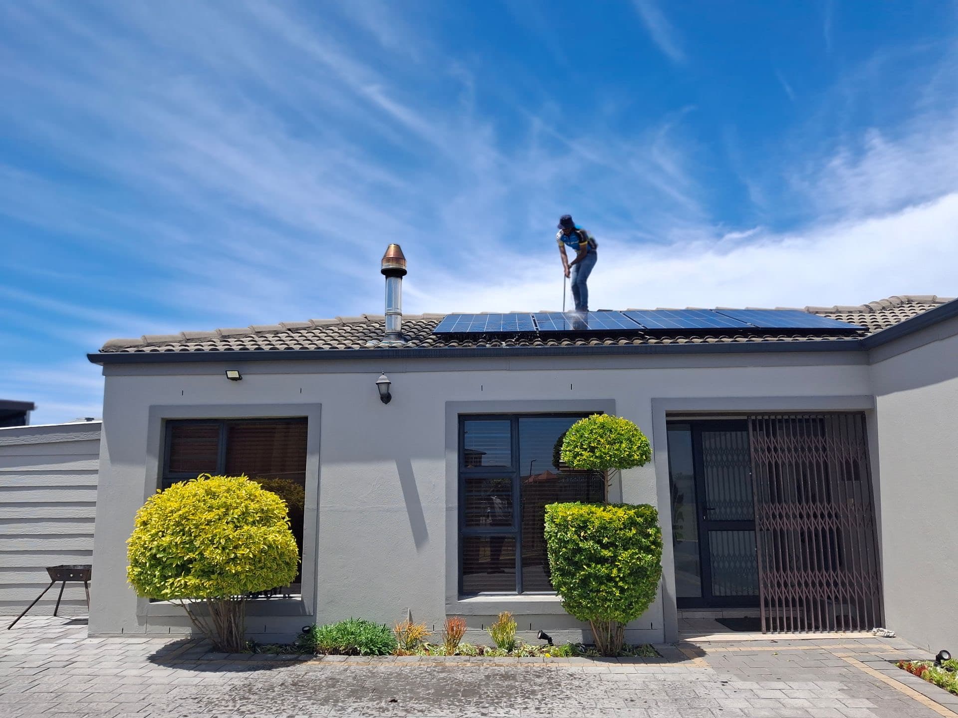Technician servicing rooftop solar panels on a home under a vivid blue sky